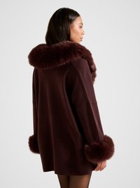 Vindika punane mantel, millel on pehme karusnahast krae ja mansetid, üle suuruse lõige ja pehme tekstuur.