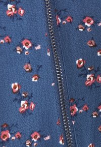 Gros plan sur un tissu bleu avec de petites imprimés floraux roses et blancs, et une fermeture éclair en métal foncé qui court verticalement au centre.