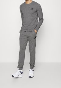 Harmaa pitkähihainen paita ja siihen sopivat collegehousut, jotka on valmistettu pehmeästä kankaasta, mustalla logolla rinnassa ja lantiolla. Yhdistetty valkoisiin lenkkareihin.