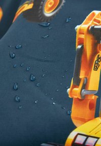 Graphique d'un véhicule de chantier jaune sur un tissu foncé avec des gouttes d'eau dispersées sur la surface.