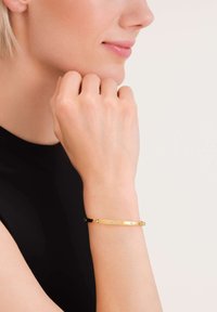 Gold-tone bracelet featuring a sleek, minimalist design with small decorative studs. Worn on a wrist, showcasing a smooth, polished texture.