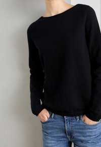 Czarny dzianinowy sweter z szerokim dekoltem i długimi rękawami, w połączeniu z niebieskimi jeansami z denimu. Miękka faktura i dopasowany krój.