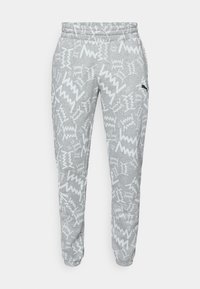 Grå sweatpants med hvide zigzag-mønstre, elastisk talje, mansjetterede ankler og et lille sort Puma-logo på højre lår.