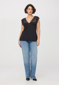 Top nero con bordo in pizzo, scollatura a V e maniche a pipistrello, abbinato a jeans a gamba larga blu chiaro. Tessuto morbido, vestibilità casual.