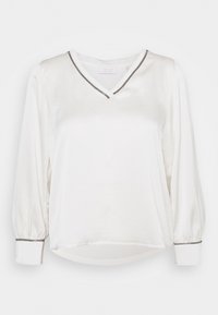 Vit blus med V-urringning, långa pösiga ärmar och en subtil grå kant längs u-ringningen och ärmsluten. Tillverkad av mjukt tyg.