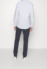 Koszula z długim rękawem w jasnoniebieskie paski z mankietami na guziki, w zestawie z ciemnoniebieskimi spodniami i białymi tenisówkami z zielonymi akcentami.