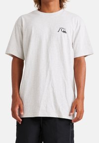 Camiseta de algodón gris claro con mangas cortas, escote redondo y un pequeño gráfico de ola en el lado izquierdo del pecho. Textura suave, corte relajado.