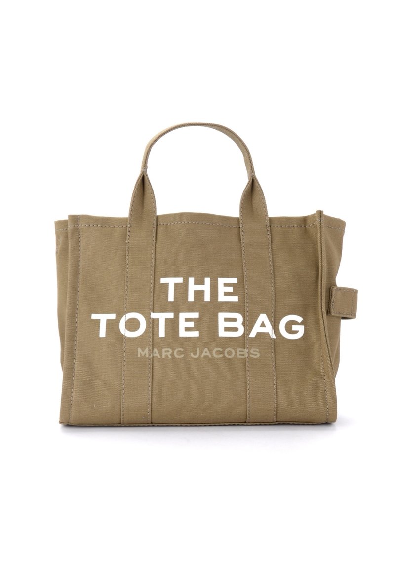 Saco de lona caqui com duas alças, com texto branco pronunciado a ler "THE TOTE BAG" e "MARC JACOBS", apresentando detalhes de costura visíveis.