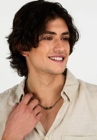 Collana in metallo con perline scure e una catena testurizzata, indossata su un collo nudo, abbinata a una camicia con colletto beige chiaro.