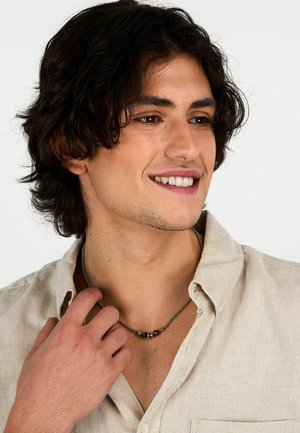 Collana in metallo con perline scure e una catena testurizzata, indossata su un collo nudo, abbinata a una camicia con colletto beige chiaro.