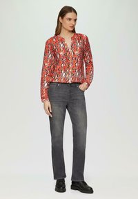 Rote Schlangenleder-Print-Bluse mit V-Ausschnitt, kombiniert mit dunkelgrauen, schmalen Jeans und schwarzen Schnürstiefeln. Glatter Stoff, lässige Passform.