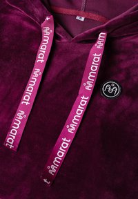 Samettihuppari syvässä purppurassa, jossa on vaaleanpunaiset nyörit ja "marat"-logo sekä pieni musta pyöreä logo-ompelu rinnassa.