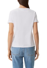 Camiseta de algodón blanca de mangas cortas con un escote redondo, que presenta un corte ligeramente relajado y una textura suave, combinada con jeans de color azul claro.