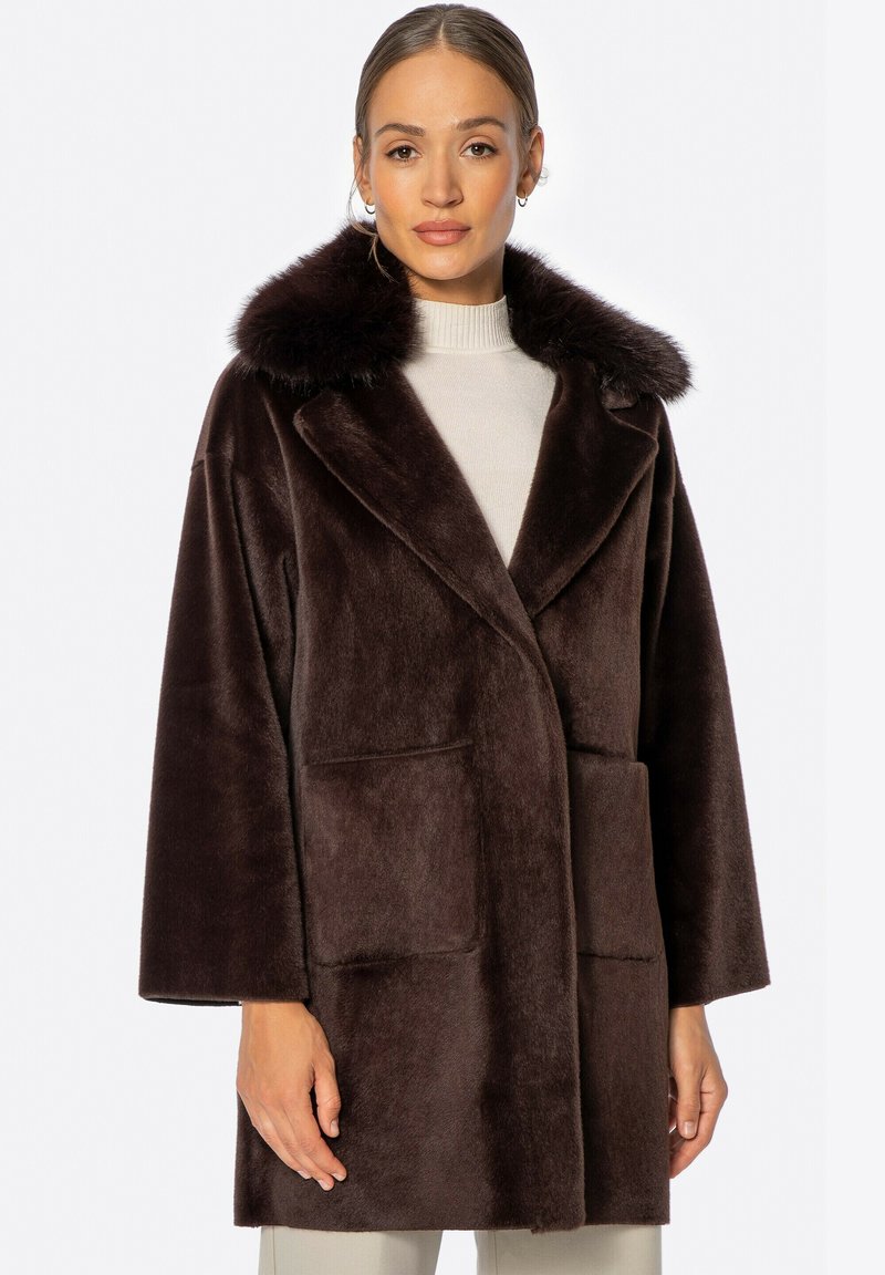 Abrigo de piel sintética marrón con un gran cuello, mangas largas y bolsillos frontales tipo parche. Textura suave con un corte relajado.