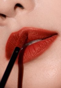 Rouge à lèvres mat rouge appliqué avec un applicateur noir sur des lèvres lisses, avec des contours définis et une texture subtile.