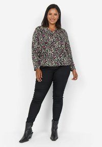 Blouse à manches longues avec une base noire présentant un motif léopard coloré en rose et blanc. Associée à un pantalon noir ajusté et des bottines.