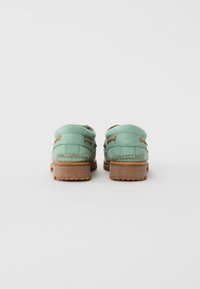 Pair of light green leather loafers with tan lace details and thick brown rubber soles, shown from the back on a plain white background.