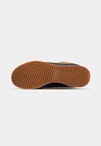 Semelle extérieure de chaussure avec semelle en caoutchouc marron présentant un motif à chevrons et un logo Nike rectangulaire embossé au centre.
