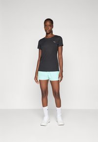 T-shirt atlético preto com mangas curtas e logótipo da PUMA, acompanhado de calções verde menta, meias brancas até ao tornozelo e sapatos atléticos brancos.