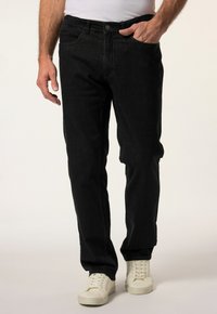 Schwarze Jeans im Straight-Leg-Schnitt, im Fünf-Taschen-Design und mit subtiler Textur. Getragen mit weißen Sneakern und einem taillierten weißen Hemd.