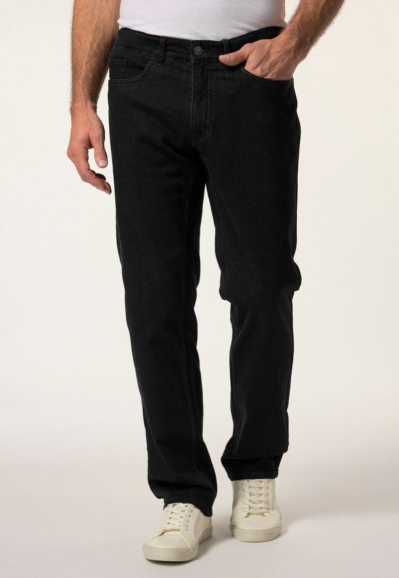 Schwarze Jeans im Straight-Leg-Schnitt, im Fünf-Taschen-Design und mit subtiler Textur. Getragen mit weißen Sneakern und einem taillierten weißen Hemd.