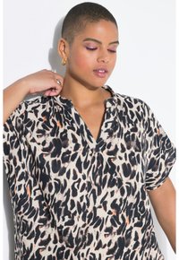 Blusa in tessuto leggero con stampa leopardata. Presenta un collo a V, maniche corte e una vestibilità comoda. I colori includono beige, nero e accenti arancioni.