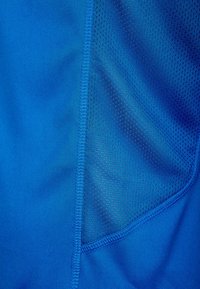 Primo piano di un tessuto blu con texture liscia e a rete, separati da una cucitura verticale con dettagli di cucitura.