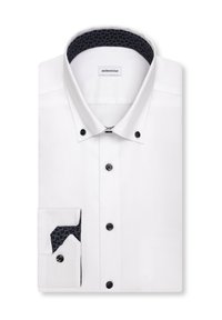 Chemise blanche à boutons avec des boutons noirs et un tissu sombre à motifs à l'intérieur du col et des poignets, soigneusement pliée avec une étiquette visible.