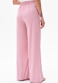 Bladoróżowe spodnie o szerokich nogawkach, gładkiej teksturze i elastycznym pasie, charakteryzujące się luźnym krojem oraz brakiem wyraźnych wzorów i elementów metalowych.