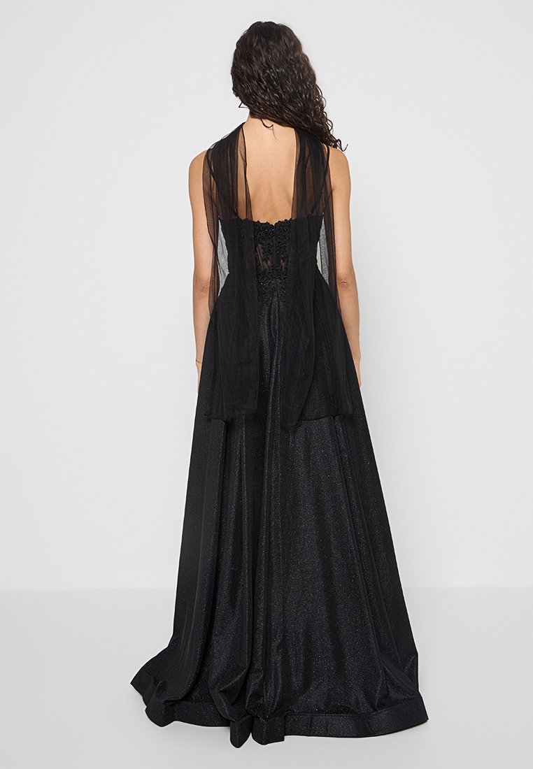 Schwarzes Abendkleid mit einem strukturierten, schimmernden Rock, transparenter Überlage und Spitzenverzierungen am Rücken. Ärmelloses Design mit tiefem V-Rücken.