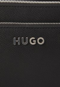 Black leather bag with a textured finish. Features a silver zipper and the embossed logo "HUGO" in polished metal.