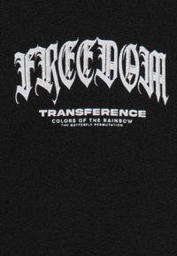 T-shirt en tissu noir avec un texte audacieux de style gothique blanc disant "FREEDOM" et "TRANSFERENCE", avec un texte plus petit en dessous. Texture lisse.