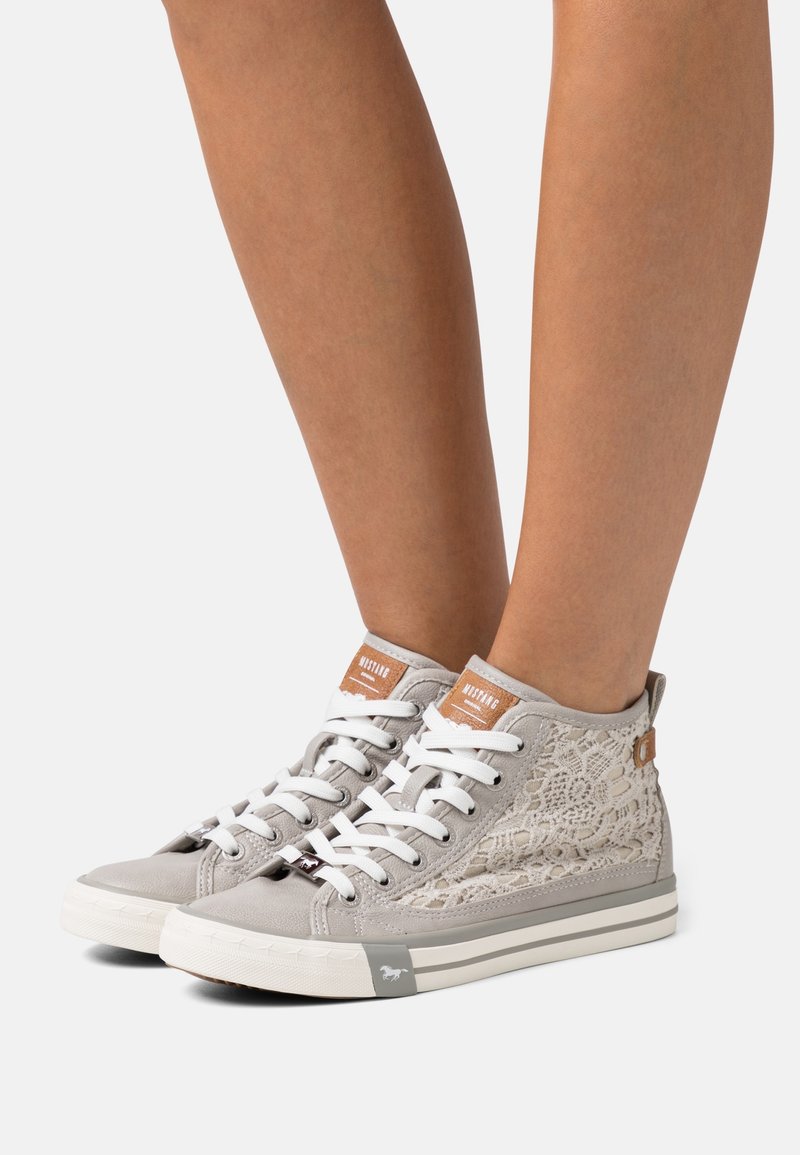 Světle šedé vysoké tenisky s texturou šněrování, bílé tkaničky a hnědé kožené akcenty. Gumová podrážka s logem na boku.