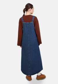 Pakaian keseluruhan denim dengan siluet melebar, tali yang dapat disesuaikan, dan hem kasar. Dipasangkan dengan kemeja lengan panjang coklat dan sepatu coklat.