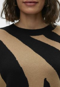 Pull en tricot avec de larges rayures noires et beiges, col rond et texture douce, mettant en avant un design moderne et contrasté.