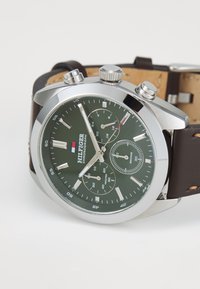 Montre chronographe pour homme avec un cadran vert, un boîtier en acier inoxydable argenté, un bracelet en cuir marron et trois sous-cadrans pour le suivi du temps.