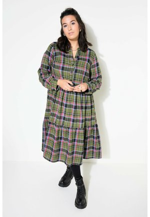 Vestido a cuadros verdes con mangas largas, cierre de botones en la parte delantera, falda de volantes, con líneas rosas y azules. Llevado con botas negras con cordones.