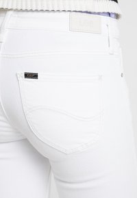 Vaqueros de mezclilla blanca con un bolsillo trasero con detalles de costura, una etiqueta de cuero en la cinturilla y una textura suave.