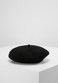 Beret de lã preto com forma redonda e plana e um design central de tufos. Textura suave, superfície lisa e sem padrões ou acessórios visíveis.