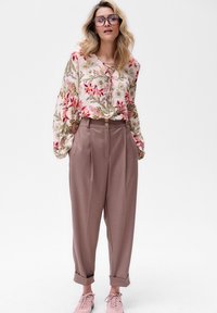 Bloem blouse in roze en groene tinten, met pofmouwen en een vetersluiting, gecombineerd met high-waisted beige broeken en roze sneakers.