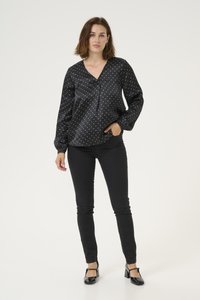 Blusa nera in raso con pois bianchi, scollatura a V e maniche lunghe a sbuffo, abbinata a jeans skinny neri e tacchi neri.