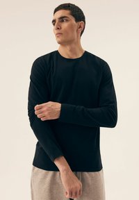 Schwarz langärmliges T-Shirt mit Rundhalsausschnitt, aus weichem Stoff, figurbetontem Design und minimalen Nähten, getragen mit hellgrauen Hosen.