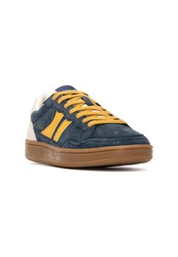 Blauwe suède sneakers met gele strepen, tan rubberen buitenzool en beige accenten. Voorzien van ronde veters en een gevoerd kraagje.