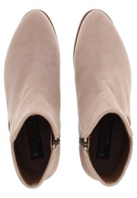 Beige mockasnörskor med en slät yta, spetsig tå och sidodragkedjor. Inuti finns en svart och färgglad sål med varumärkesetikett.