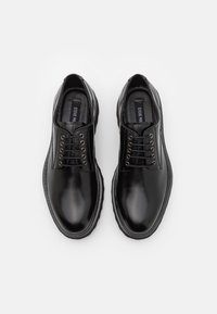 Chaussures habillées en cuir noir à finition lisse, bout rond, semelle surélevée et œillets pour les lacets. Présentent une étiquette de marque à l'intérieur.