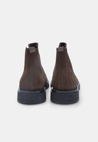 Stivaletti in suede marrone con suola in gomma testurizzata bassa e pratica linguetta sul retro, caratterizzati da un design leggermente affusolato.
