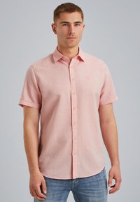Camisa de botones de manga corta en tejido rosa claro con una textura sutil; presenta un collar, cierre frontal de botones y un pequeño detalle de logo.