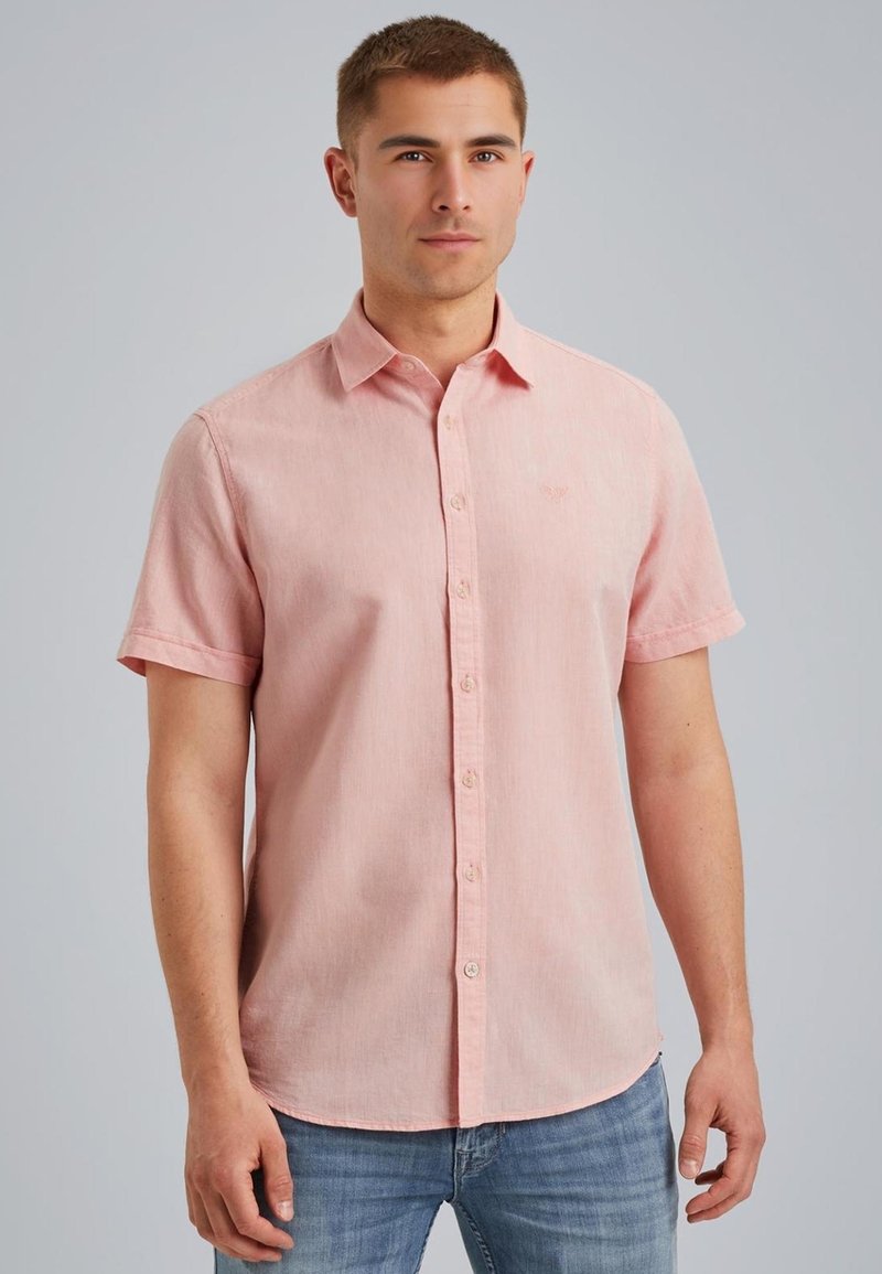 Camisa de botones de manga corta en tejido rosa claro con una textura sutil; presenta un collar, cierre frontal de botones y un pequeño detalle de logo.