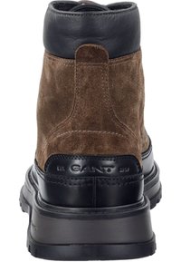 Bruine suède enkelboot met een zwarte leren kraag en contrasterende zwarte rubberen zool; voorzien van gebosselde branding en stiksels.