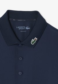 Marinblå piké i regular fit, med klassisk krage, tre knappar samt en grön krokodillogo med röd accent.